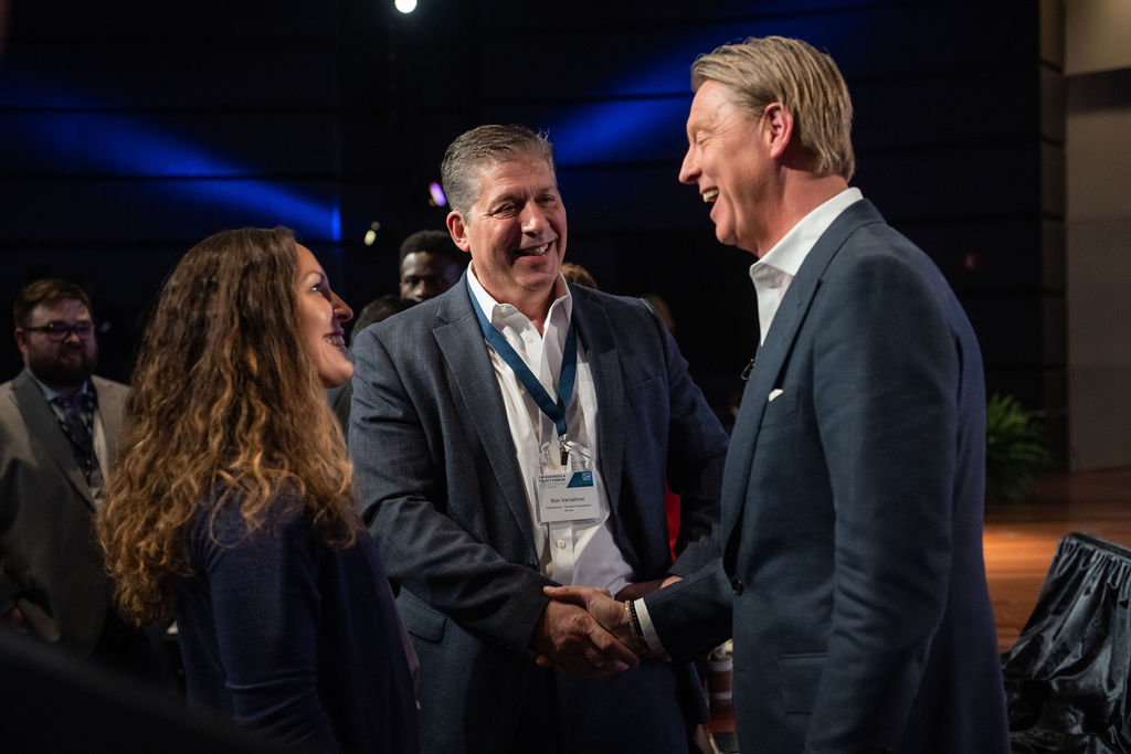 Three people in suits smiling two of them shaking hands