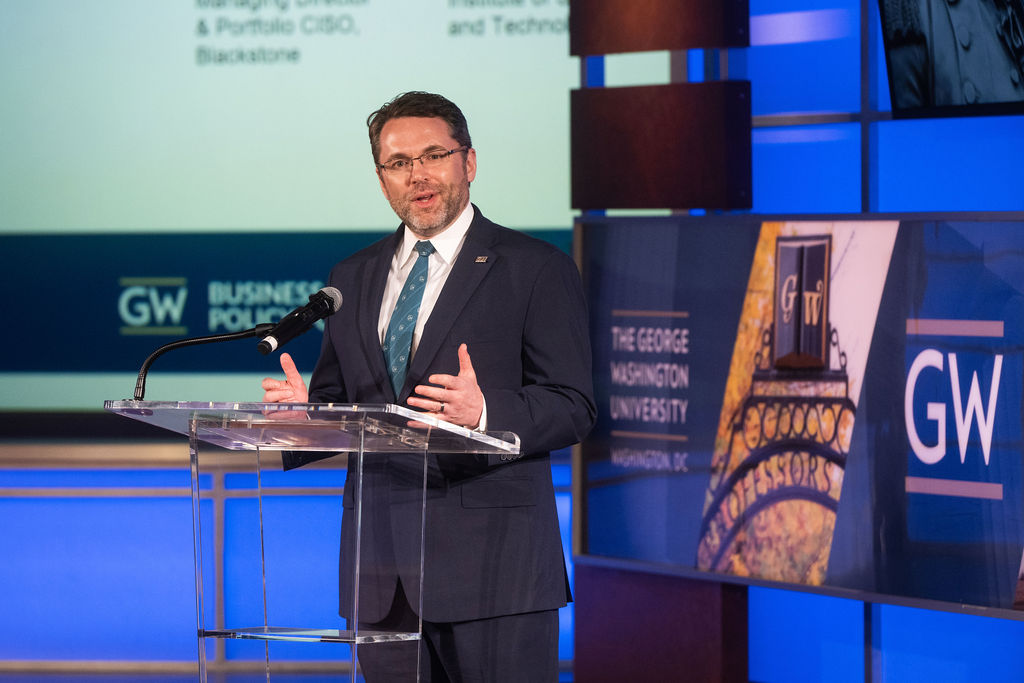 man speaking at podium with geroge washington university signs in the background